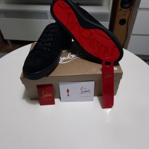 Svarta sneakers från Christian Louboutin - Snygga svarta sneakers i mocka från Christian Louboutin med klassisk röd sula och svarta skosnören. Låg modell med stilren design och diskreta detaljer. Perfekta för dig som vill ha något exklusivt och trendigt.