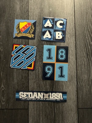 Klistermärken Djurgården fotboll - Säljer ett set med klistermärken med Djurgården-tema. Motiven inkluderar DIF-loggan, texten ACAB, siffrorna 1891 och grafiska mönster i blått, vitt, gult och rött. Perfekt för att dekorera laptop, vägg eller andra ytor.