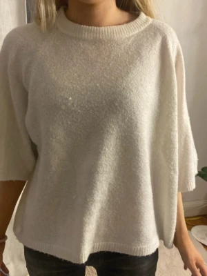 Vit stickad tröja - Mysig vit stickad tröja med oversized passform och trekvartsärmar. Tröjan har rund halsringning och är tillverkad i ett mjukt, fluffigt material som ger en avslappnad look.