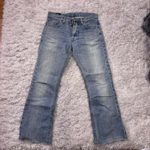 Ljusblå raka jeans med slitning - Säljer ett par ljusblå jeans med rak passform och en tydlig slitning vid ena knät. Jeansen har klassisk femficksdesign, normal midja och är tillverkade i denim. Perfekta för en avslappnad och trendig look.