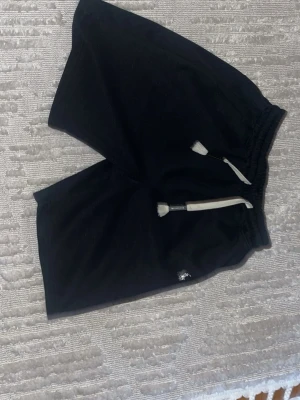 Svarta raplhlaurenshorts - Säljer ett par svarta shorts med vit snörning i midjan och elastisk resår. Shortsen har en avslappnad passform och är perfekta för chill dagar. Liten logga på ena benet. Sköna och stilrena för sommaren. Helt nya 