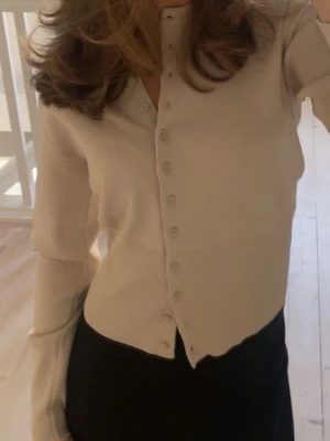 Beige cardigan från Zara - Stilren beige cardigan från Zara med rund halsringning och knappar framtill. Tröjan har långa ärmar och bred ribbstickad kant nedtill och vid ärmsluten. Perfekt att slänga över en topp för en enkel och snygg look.