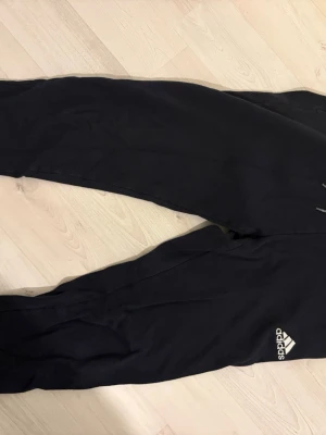 Svarta mjukisbyxor från Adidas - Säljer ett par svarta mjukisbyxor från Adidas med klassisk logga på benet. Byxorna har resår i midjan och är gjorda i mjukt material som passar perfekt för chill dagar. Snygg och enkel design som funkar till det mesta.