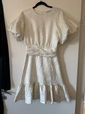 Studentklänning - Helt ny klänning med prislappen kvar, säljer den då jag redan har en studentklänning. Från Neo Noir. Vollang nedtill, ballongärmar, lång dragkedja i ryggen, går in i midjan och mönster av blommor. Gräddvit. Perfekt som studentklänning eller som en sommarklänning. 