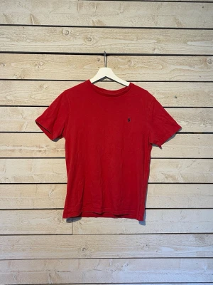 Röd t-shirt från Ralph Lauren - Klassisk röd t-shirt från Ralph Lauren med liten broderad logga på bröstet. T-shirten har rund halsringning och korta ärmar. Tillverkad i mjuk bomull för en skön känsla och enkel stil.