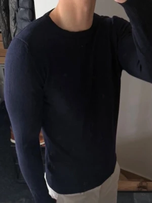 Mörkblå rundhalsad tröja - Snygg mörkblå tröja från J.Lindeberg med rund halsringning och långa ärmar. Tillverkad i mjukt material som sitter skönt på kroppen. Perfekt basplagg för en stilren look. 100% merinoull. Storlek m men är liten i storlek. Så sitter som xs