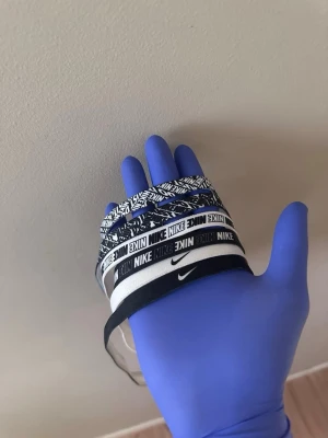Nike elastiska hårband svart/vit - Säljer ett set med fem elastiska hårband från Nike i svart och vitt. Hårbanden har olika mönster och loggor, vissa med grafiskt tryck och andra med klassisk Nike-text. Perfekta för att hålla håret på plats under träning eller till vardags.