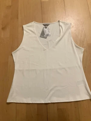 NY Vit v-ringad linnetopp från H&M storlek XL - Säljer en enkel och stilren vit linnetopp från H&M. Toppen har v-ringning och är ärmlös, perfekt för varma dagar eller som layering-piece. Tillverkad i mjukt och lätt material som känns skönt mot huden. Helt ny med prislappen kvar, storlek XL