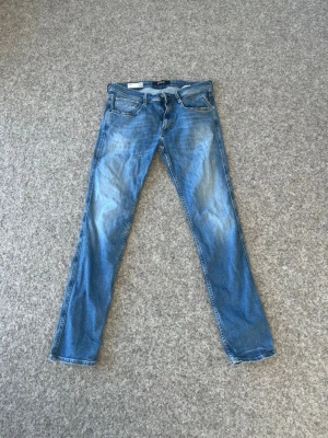 Blå raka jeans från Replay - Säljer ett par klassiska blå jeans från Replay med raka ben och snyggt slitna detaljer. Jeansen har fem fickor, normal midja och är gjorda i bomull. Perfekta för en avslappnad och trendig look. Byxorna är inköpta för 1499kr och jag säljer dessa för 159kr pågrund av hemma sydd där bak vid bakfickan. Skriv om du har någon fråga.