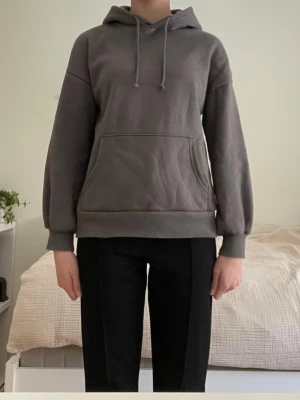 Mörkgrå hoodie  - En stilren mörkgrå hoodie med huva och dragsnören. Hoodien har en stor magficka framtill och ribbade muddar vid ärmslut och nederkant. Perfekt för en avslappnad och casual look. Materialet är mjukt och bekvämt, troligen bomullsblandning. Den sitter jättebra och säljer då jag har vuxit ur den, superskön hoodie!