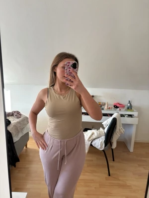 Beige body - Säljer en stilren beige body med rund halsringning och ärmlös design. Bodyn har en tight passform och är tillverkad i ett stretchigt material som sitter snyggt mot kroppen. Perfekt att matcha med olika underdelar för en enkel och clean look. Aldrig använd!