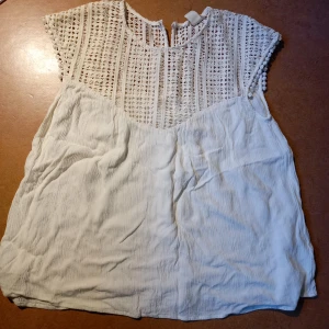 Vit blus - Vit blus som är väldigt söt och fin. Halvt genomskinlig ovanför brösten, sedan ett flowy tyg. Knäpper med en knapp i nacken, så den sitter snyggt och propert om halsen. Storlek 36 men kan passa lite större oxå. 🤍