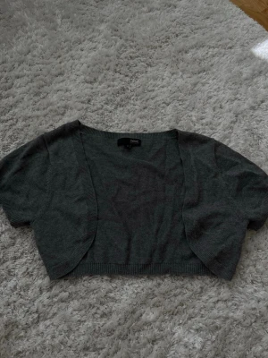 Grå bolero från Next Petite - Kort grå kofta från Next Petite med öppen front och ribbade kanter. Perfekt att slänga över en topp för en enkel och stilren look. Mjuk och tunn stickning som passar till många outfits.