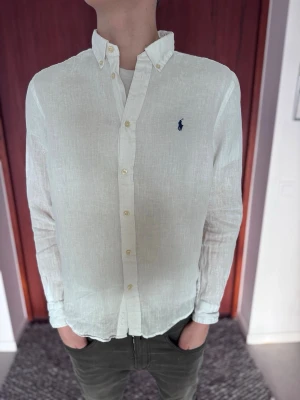 Polo Ralph Lauren Linneskjorta – Vit (HELT NY) - Helt ny och oanvänd vit långärmad linneskjorta med marinblå logga. Det perfekta sommarplagget! Det är den största barnstorleken som motsvarar en Small i herr. Krispigt vit och aldrig använd. • Märke: Polo Ralph Lauren • Material: 100% Linne • Storlek: Barn XL (Passar herr Small) • Nypris: ca 1 500 kr • Skick: Helt ny / Nyskick 