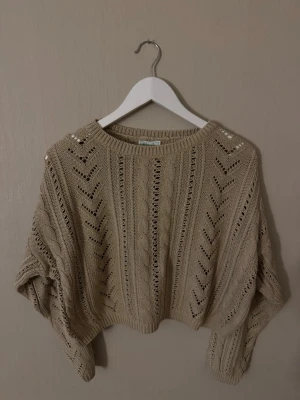 Vintage Benetton stickad tröja 80s/90s - Trendig beige croppad stickad tröja med hålmönster och kabelstickade detaljer. Perfekt för lager på lager och ger en avslappnad men snygg look. Bredden: 63cm (armhåla till armhålan)Längden:44cm