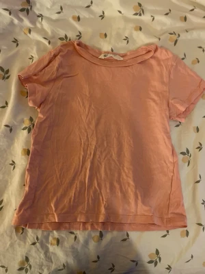Ljusrosa t-shirt från H&M barn st 122/128 - Enkel och mjuk ljusrosa t-shirt från H&M med rund halsringning och korta ärmar. Tillverkad i bomull. Barn storlek 122/128 