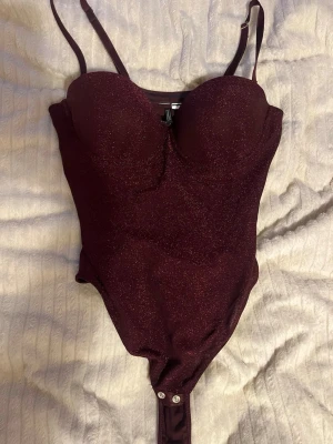 Vinröd glittrig body från Intimissimi - Säljer den här fina och festliga bodyn från intimissimi. Passar så bra till en fest. Använd en gång då den var lite liten vid bysten. 