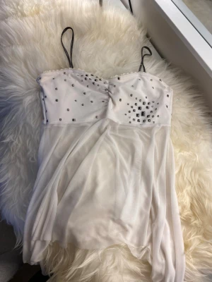 Vitt nattlinne med strassdetaljer - Säljer ett vitt nattlinne med tunna axelband och glittriga strassdetaljer över bysten. Nattlinnet är gjort i ett tunt, transparent tyg som ger en luftig känsla. Perfekt för dig som vill ha något extra fint att sova i.