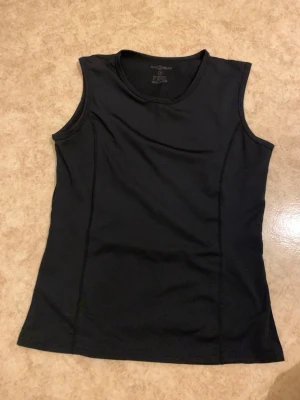 Svart ärmlös linnetopp - Säljer en svart, enkel och sportig linnetopp. Toppen är ärmlös och har en rund halsringning. Perfekt för träning eller som basplagg till olika outfits.