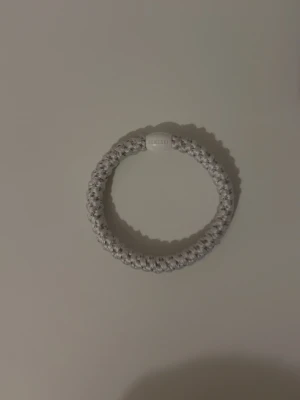 Vit flätad hårsnodd från kknekki - Säljer en vit flätad hårsnodd från Kknekki. Hårsnodden är rund och har en vit plastdetalj med logga. Perfekt för att hålla håret på plats och ger en snygg detalj till din frisyr.