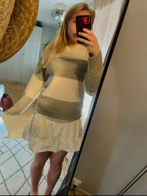 Randig stickad tröja i grönt och vitt - Mysig stickad tröja med breda ränder i ljusgrönt och vitt. Tröjan har rund halsringning, ribbstickad struktur och långa ärmar. Perfekt för lager på lager och enkel att matcha med olika outfits. Lite nopprig vilket syns på andra bilden men fortfarande bra skick!