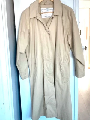 Beige trenchcoat med klassisk krage vintage  - Stilren beige trenchcoat , vintage, med klassisk bred krage och raka ärmar. Lång modell med två sidofickor och dold knäppning framtill. Tillverkad i ett slätt tyg som ger en clean look. Perfekt för dig som gillar minimalistisk och tidlös stil.