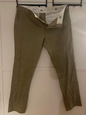 Beiga chinos från Dickies - Säljer ett par klassiska beiga chinos från Dickies med raka ben och bälteshällor. Byxorna har två fickor fram och två bakfickor, varav en med knapp. Tillverkade i ett slitstarkt bomullsmaterial som ger en clean och stilren look.