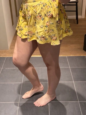 Gul blommig byxkjol med volang - Dags för någon annan att njuta av dessa. Säljer en gul byxkjol med blommigt mönster och volangkant. Den har hög midja med resår och är tillverkade i ett lätt och luftigt tyg, perfekta för varma dagar. Passformen är loose och shortsen har en somrig vibe. Det 100% bomull och i fantastiskt skick