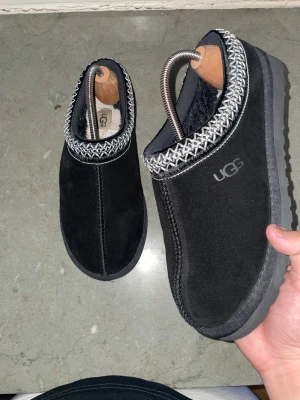 Svarta UGG tofflor med mönstrad kant - Säljer ett par svarta UGG tofflor i nytt skick. Klassisk UGG-logga på sidan. Dem är extremt sköna och passar till de mesta.