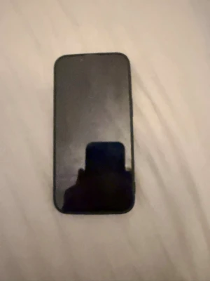 Svart iPhone 13 - Säljer en svart iPhone med stilren design och rundade hörn. Telefonen har två kameror på baksidan och en slimmad form. Tillverkad i glas och metall, perfekt för dig som gillar Apples klassiska look. Som ni ser på bilden har den fått lite smällar men man ser inget med skalet på