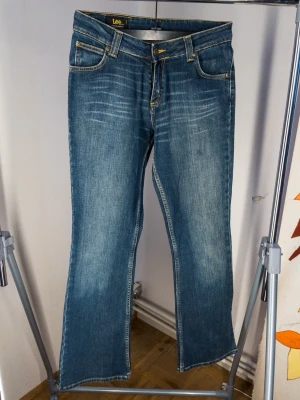 Blå bootcut jeans från Lee - Säljer ett par klassiska blå bootcut jeans från Lee med snygga slitningar och kontrastsömmar. Jeansen har fem fickor och gylf med dragkedja. Tillverkade i slitstark denim som ger en tidlös look.
