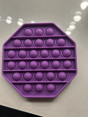 Lila pop it i silikon, åttakantig - En lila pop it-leksak i mjukt silikon med åttakantig form. Perfekt för att stressa ner eller bara ha något att pilla på. Bubblorna kan tryckas ner och ger ett tillfredsställande popp-ljud. Enkel att ta med sig och använda överallt.