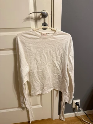 Vit långärmad croppad topp från Nelly - Säljer en vit långärmad topp från Nelly med knytband i ryggen. Använd 1 gång, storlek XXS. 