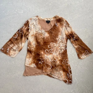 Whimsy topp - Unik topp med blommigt broderi och asymmetrisk nederkant. Blusen har trekvartsärm, v-ringning och ett coolt batikmönster!❤️