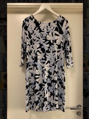 Fin klänning - Snygg klänning med vita/blå blommor och trekvartsärm. Klänningen har en rak passform och är tillverkad i ett mjukt, lätt material som känns skönt mot huden. Perfekt för dig som gillar stilrena mönster och vill ha något som sticker ut.