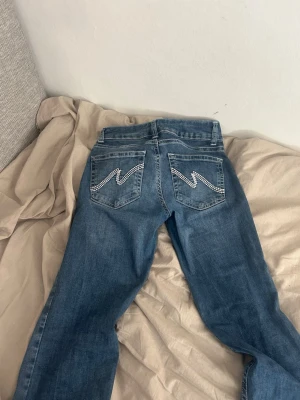 Blå bootcut nelly jeans  - Säljer ett par blå bootcut jeans med snygga broderade detaljer på bakfickorna. Jeansen har klassisk femficksdesign och är tillverkade i ett mjukt denimtyg. Perfekta för dig som gillar en avslappnad men ändå trendig stil. skriv för fler frågor!