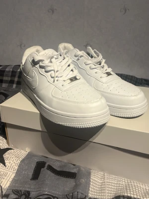 Nike Air Force 1 vita sneakers - Klassiska helvita Nike Air Force 1 sneakers i lågt utförande. Skorna har en stilren design med perforerad tå, kraftig sula och ikoniska swoosh-loggan på sidan. Tillverkade i läder med vita skosnören och detaljer. Perfekta för en clean och tidlös look.