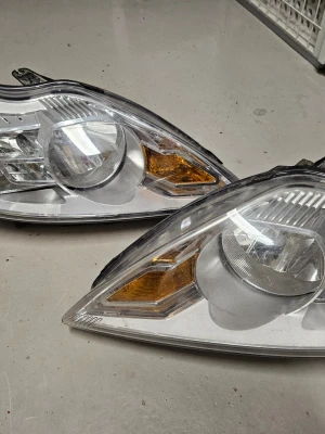 Bilstrålkastare i klarglas - Säljer ett par bilstrålkastare med klarglas och inslag av orange blinkers. Strålkastarna har en modern, trekantig form och är tillverkade i plast och metall. Passar till dig som vill byta ut eller uppgradera bilens belysning.. är till ford focus år 08-11