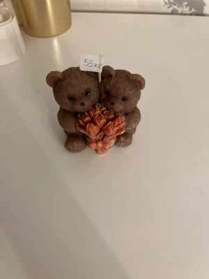 Dekorationsfigur björnar med blommor - Söt liten dekorations doftljus föreställande två bruna björnar som håller i en bukett orange blommor. . Perfekt som prydnad på hyllan eller skrivbordet.