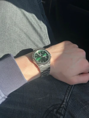 Silverfärgad Black Oak klocka grön urtavla - Stilren klocka från Black Oak med silverfärgat armband i metall och en snygg grön urtavla. Klockan har en rund boett med detaljerade skruvar och datumvisning. Perfekt accessoar för dig som vill sticka ut med en modern look. Helt ny aldrig använt. Ny pris 800kr. Går att buda.