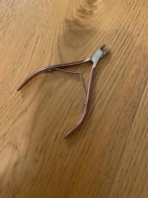 Nagelbandsklippare i metall - Nagelbandsklippare i rostfritt stål med böjda handtag och fjäder för smidig användning. Perfekt för att trimma nagelband och små detaljer vid manikyr. Handtagen har en roséguldig ton och verktyget är kompakt och lätt att hantera.