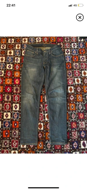 Mörkblå raka jeans från Nudie Jeans - Säljer ett par mörkblå  jeans från Nudie Jeans med klassisk femficksmodell och raka ben. Jeansen har subtila slitningar och kontrastsömmar. Tillverkade i denim av bomull, perfekta för en avslappnad och stilren look.