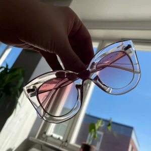 Cat eye solglasögon med rosa glas - Snygga solglasögon med transparent båge i cat eye-modell och rosa tonade glas. Perfekt accessoar för att lyfta din stil med en cool och trendig vibe. Bågarna är i plast och har en modern, stilren design.