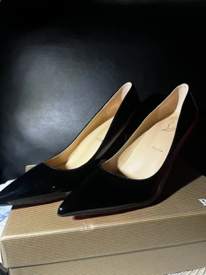 Svarta louboutin klackar - Säljer ett par klassiska svarta pumps i lack. Skorna har spetsig tå, hög smal klack och den ikoniska röda sulan. Insidan är beige och materialet är glansigt läder. Perfekta för dig som vill ha en elegant och tidlös look.