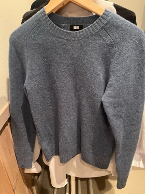 Blå stickad tröja från Uniqlo - Mysig blå stickad tröja från Uniqlo med rund halsringning och ribbade muddar vid ärmslut och nederkant. Tröjan har en enkel och klassisk design som passar perfekt till lager på lager. Tillverkad i mjukt material för extra komfort.
