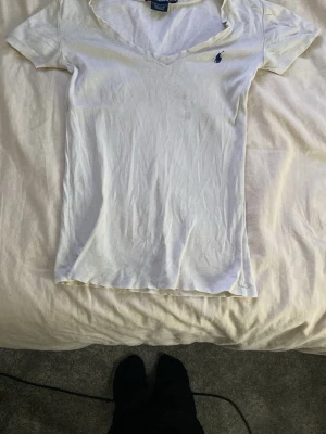 Vit t-shirt från Polo Ralph Lauren - Klassisk vit t-shirt från Polo Ralph Lauren med v-ringning och korta ärmar.  Tillverkad i mjuk bomull som känns skön mot huden. Perfekt basplagg för en clean och enkel stil. Den matchar med allt och är väldigt fin på kroppen 💗Öppen till alla prisförslag💕