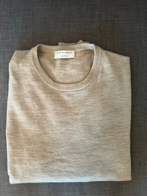 Beige tröja från Tiger of Sweden - Snygg beige tröja från Tiger of Sweden i modellen MATIAS. Tillverkad i 100% merino ull med rund hals och långa ärmar. Perfekt för en clean och stilren look. Skicket är bra förutom tre små hål uppe på axeln och i nacken, (de är en hund som bitit). Men de syns inte så mycket speciellt om man har en vit t shirt under. Bara att skriva om ni vill ha fler bilder eller har funderingar.