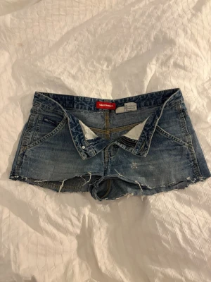 Blå jeansshorts från Unionbay - Säljer ett par klassiska blå jeansshorts från Unionbay. Shortsen har låg midja, knappgylf och slitna detaljer. Sitter som S 