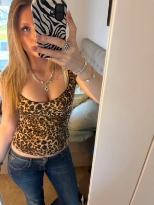 Leopardmönstrad topp med smala axelband - Snygg leopardmönstrad topp med smala axelband och djup urringning. Toppens material känns stretchigt och sitter tight mot kroppen. Perfekt för dig som vill sticka ut med ett djuriskt mönster.