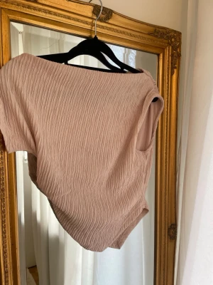 Beige ärmlös linnetopp i crinkletyg - Oanvänd Storlek S kan även passa XS, en linnetopp med crinklad struktur. Toppen har en avslappnad passform och rund halsringning, Materialet känns lätt och luftigt, vilket 